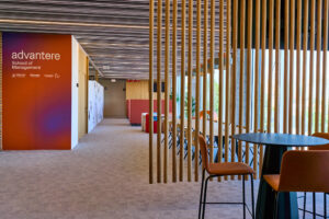 Fotografía corporativa de reportaje de las instalaciones modernas de Advantere School of Management en Madrid. Muestra un pasillo luminoso y un área de co-working con diseño de lamas de madera. Ideal para imagen de marca y facilities.
