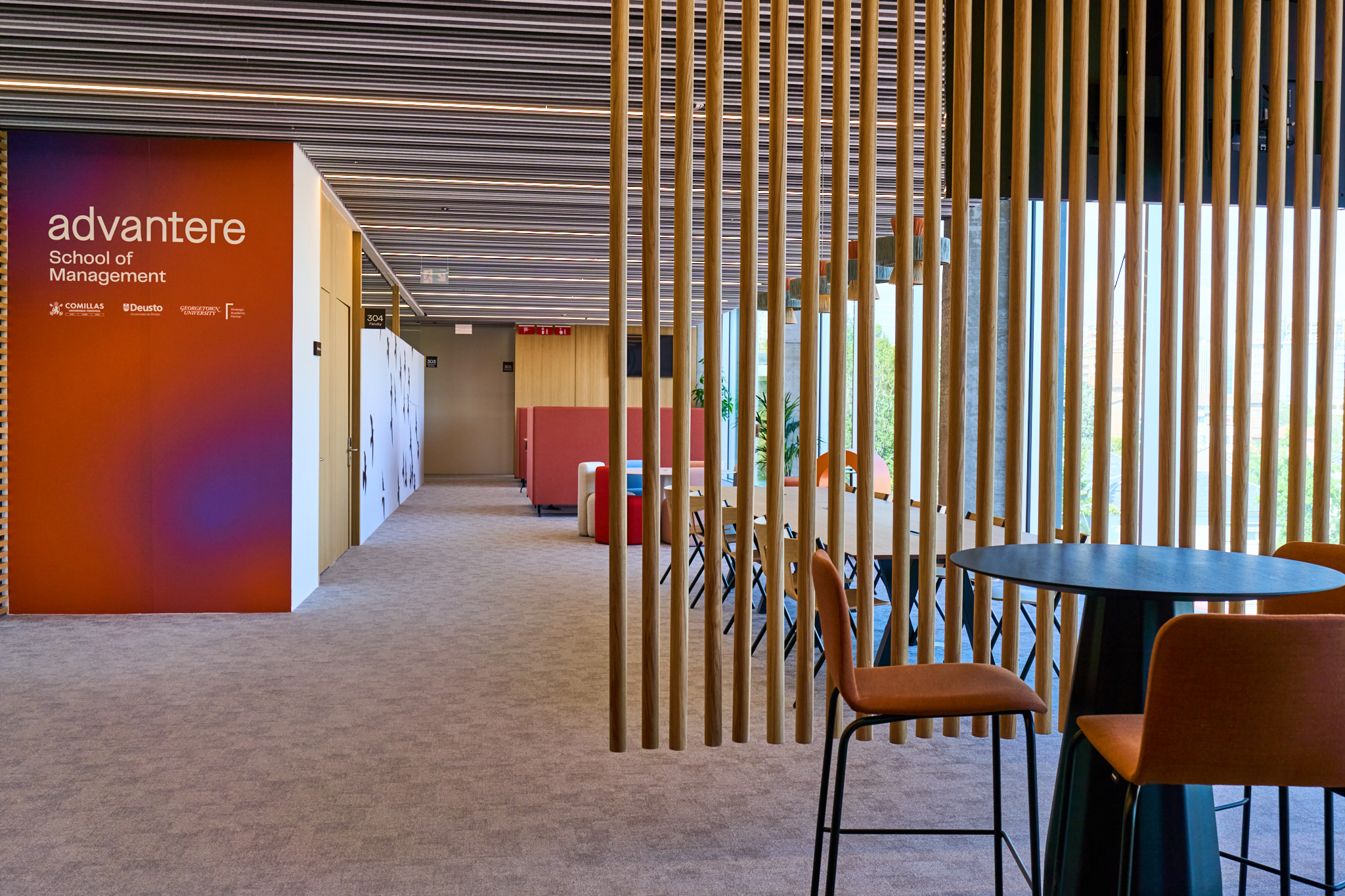 Fotografía corporativa de reportaje de las instalaciones modernas de Advantere School of Management en Madrid. Muestra un pasillo luminoso y un área de co-working con diseño de lamas de madera. Ideal para imagen de marca y facilities.
