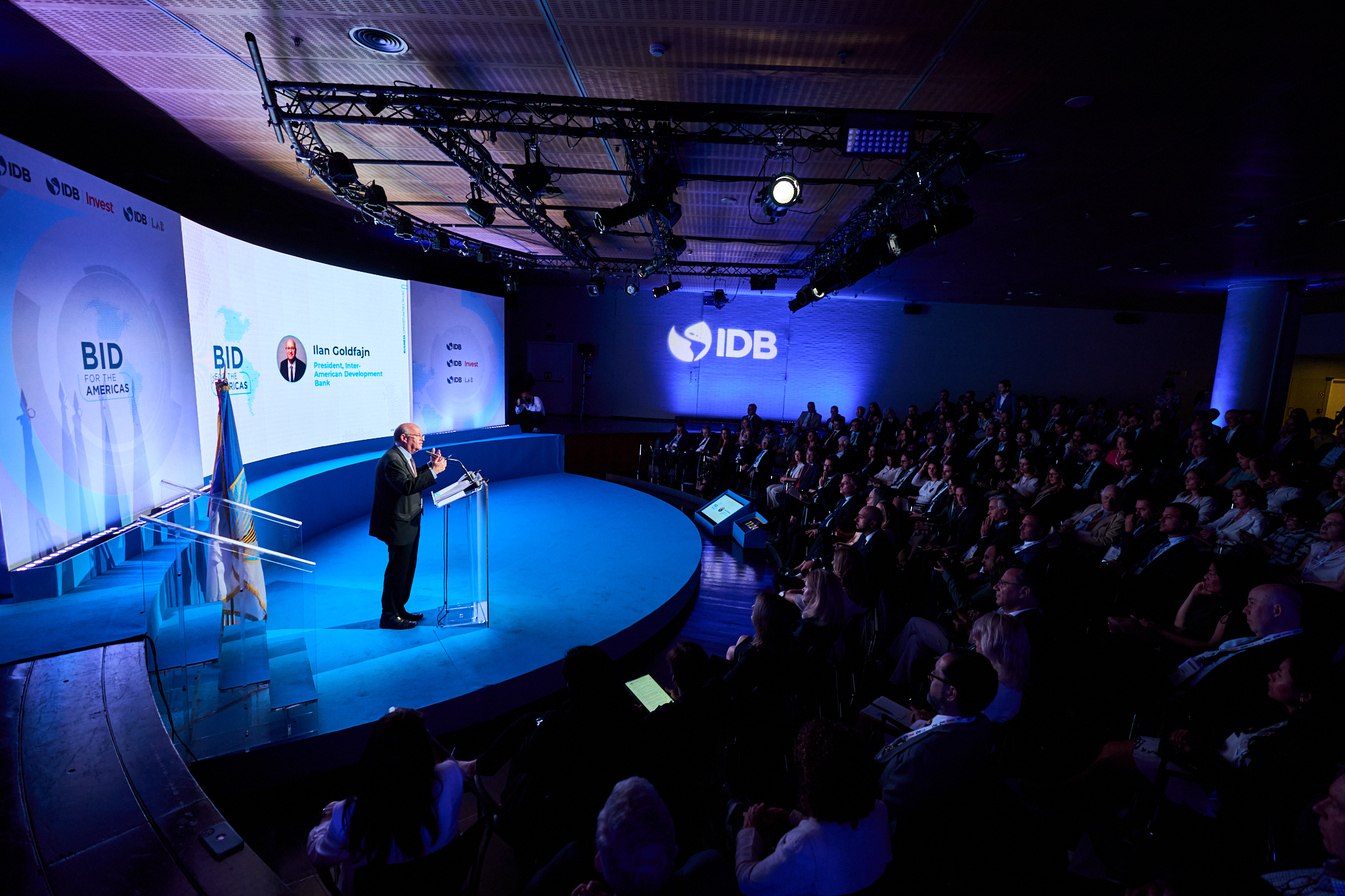 Fotógrafo profesional en Madrid cubriendo el congreso BID for the Americas. Muestra el escenario principal y el auditorio con iluminación azul. Se ve al ponente y la producción de un evento de gran formato.