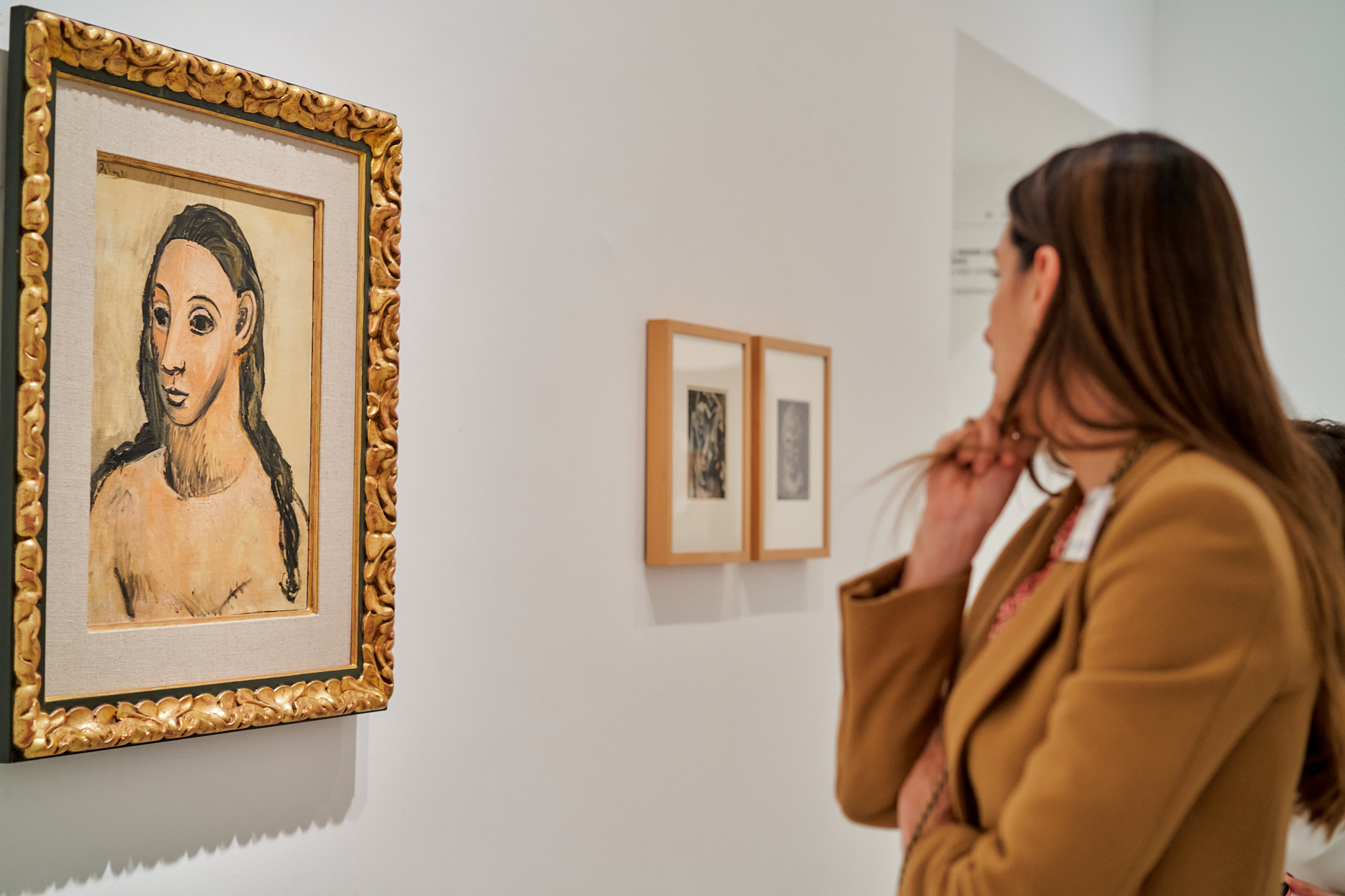 Fotógrafo de eventos en Madrid cubriendo un evento cultural o visita de empresa a un museo o galería. Muestra a una mujer mirando un cuadro enmarcado con un marco dorado sobre una pared blanca. Ideal para reportaje de marca en un contexto artístico
