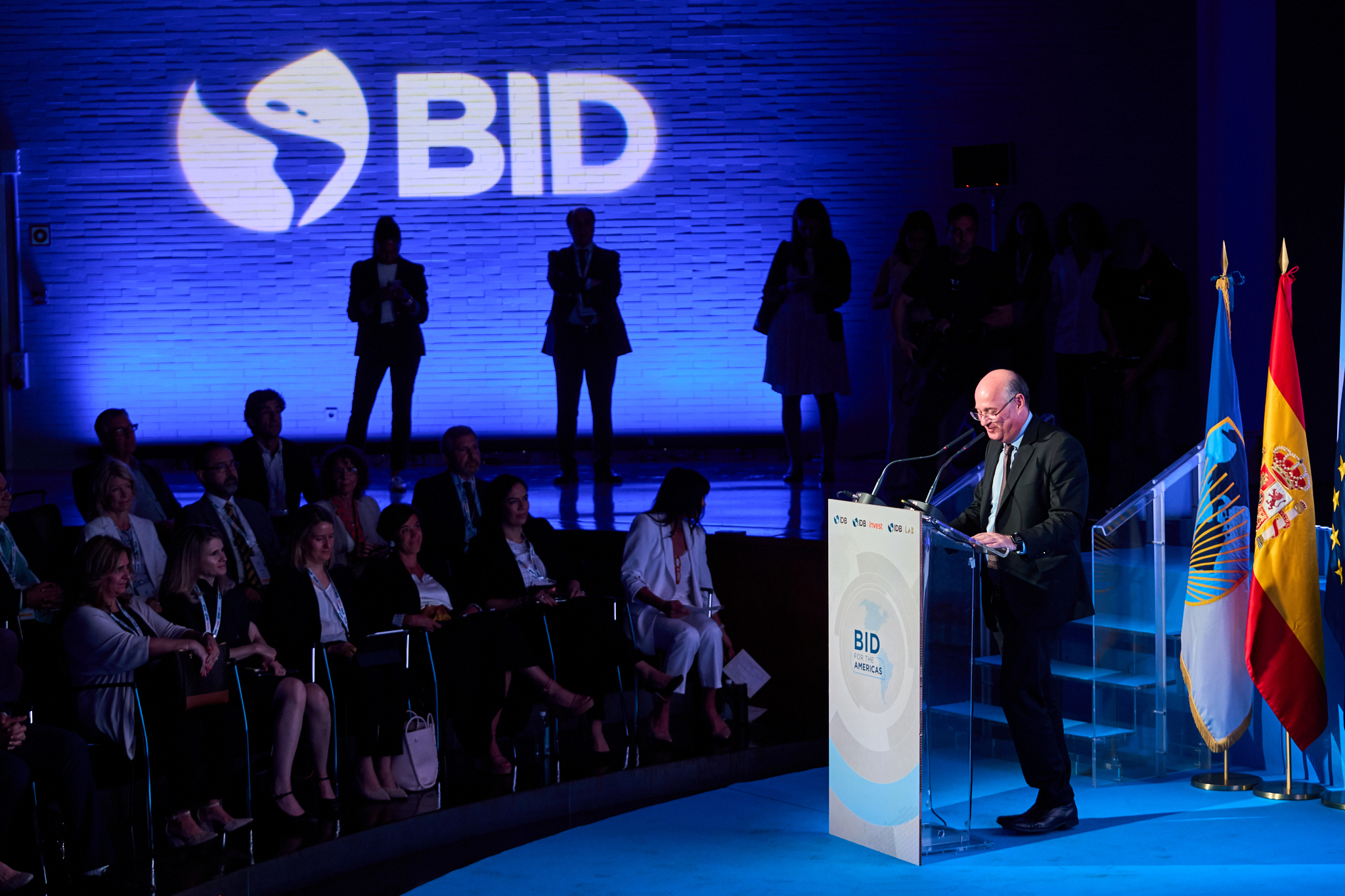 Fotógrafo profesional en Madrid cubriendo el evento BID for the Americas. Muestra a un ponente principal en el podio ante el logo del BID y banderas. Ideal para cobertura de grandes congresos y jornadas institucionales.