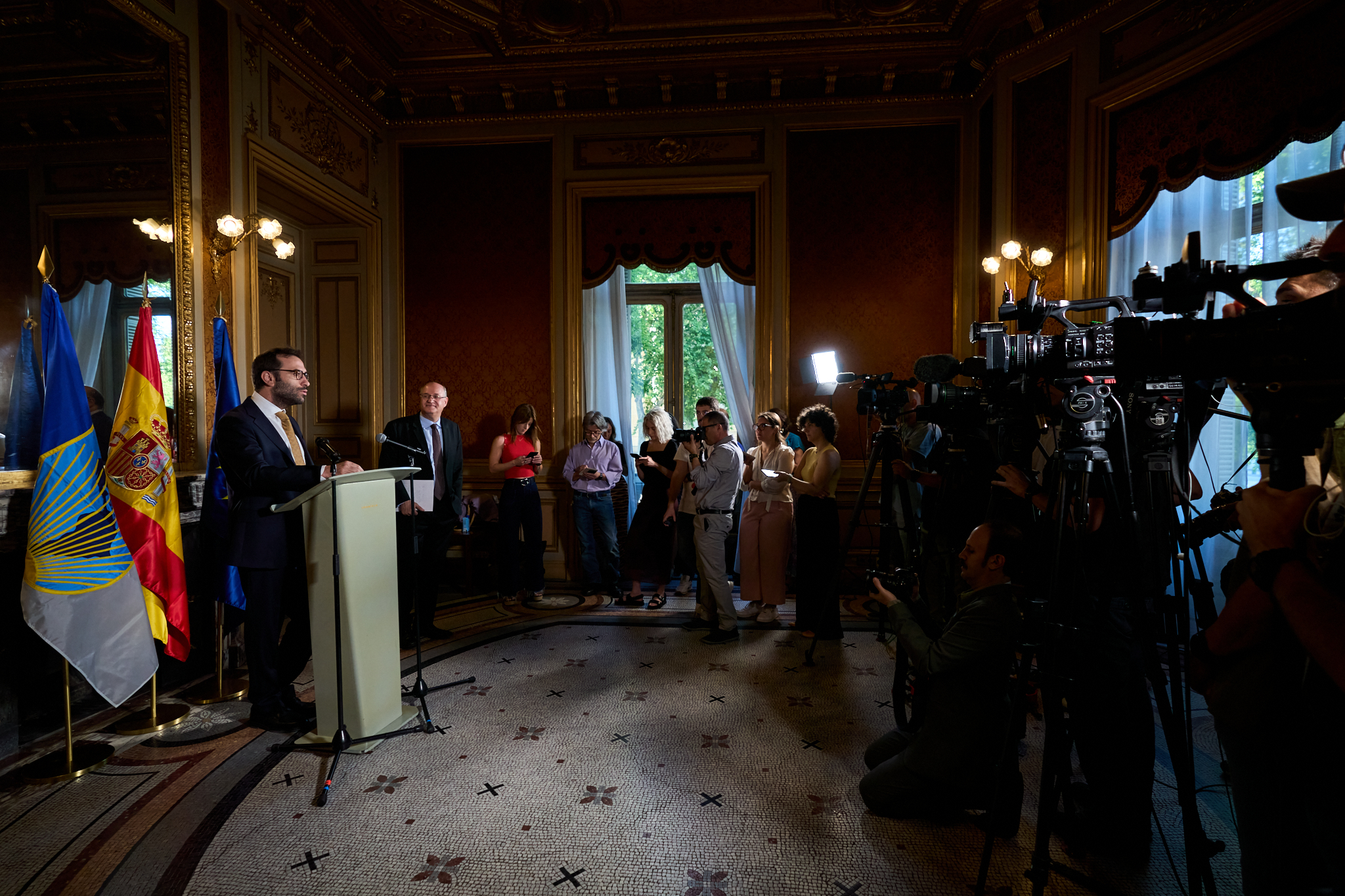 Fotógrafo profesional en Madrid cubriendo una Rueda de Prensa Institucional. Muestra a un ponente en el podio, con banderas de España y Madrid, rodeado de cámaras de prensa y periodistas. Ideal para cobertura de eventos de comunicación y corporativos.