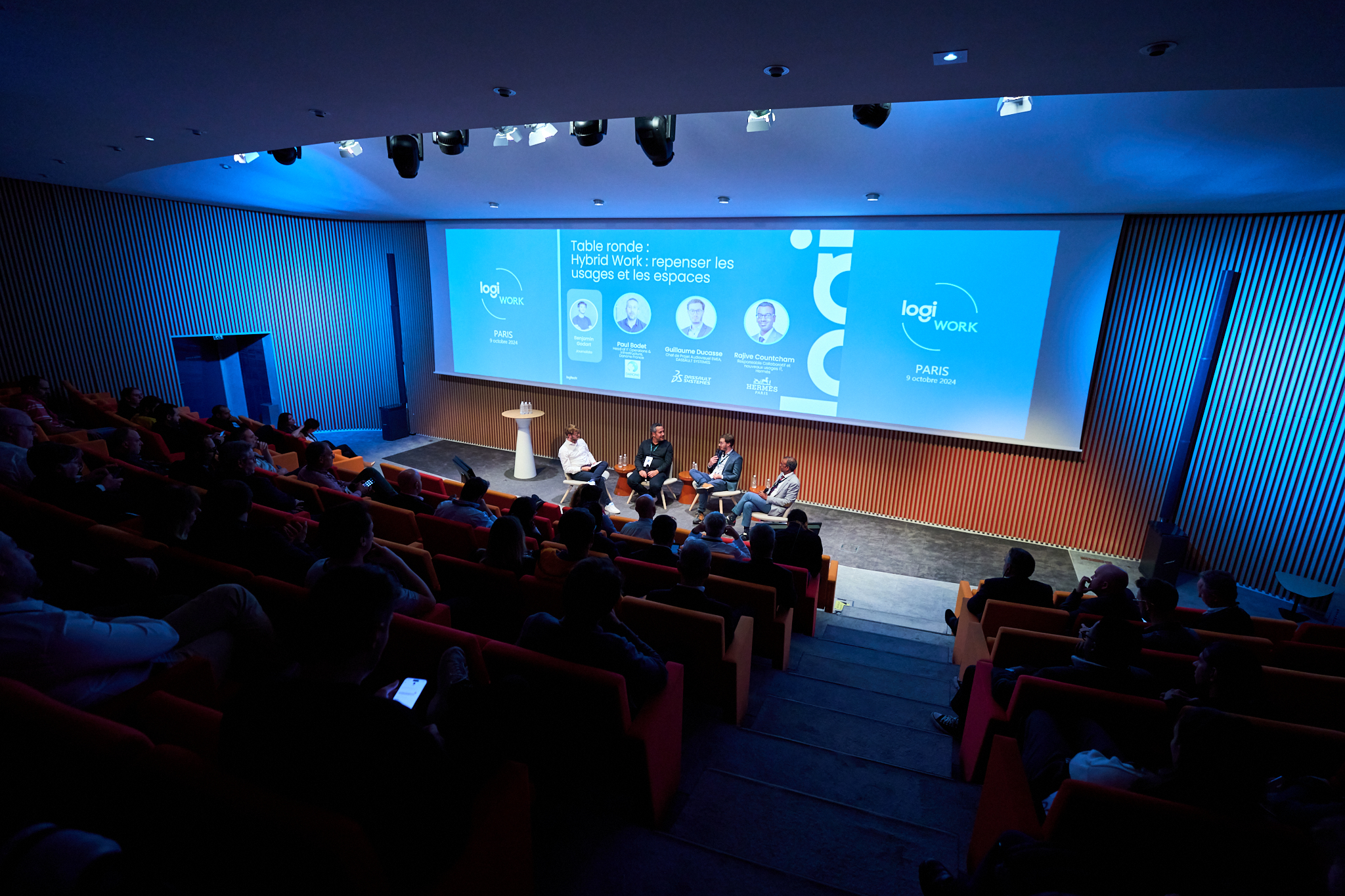 Reportaje fotográfico de congreso o jornada. Fotógrafo profesional en Madrid cubriendo un panel de debate para Logi Work (Logitech). Muestra la sala de conferencias con los ponentes y una audiencia completa, ideal para servicios de fotografo para empresas.