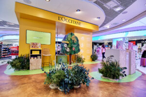 Fotografía de reportaje de stand promocional de L'Occitane en el aeropuerto de Madrid (Duty-Free). Muestra un diseño temático con elementos naturales, plantas y tonos amarillos. Ideal para cobertura de ferias, pop-up stores y activaciones de marca.
